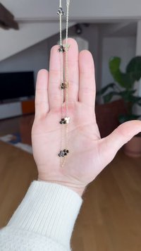 Naszyjnik z łańcuszka złotego z trzema ozdobami w kształcie kwiatów, z czarnym kamieniem szlachetnym w centrum każdego z nich. Trzymany w dłoni do porównania rozmiaru.