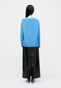 Μπλε πλεκτό πουλόβερ με στρογγυλή λαιμόκοψη, συνδυασμένο με μαύρη δερμάτινη μάξι φούστα με πίσω σκίσιμο και ψηλοτάκουνα παπούτσια.