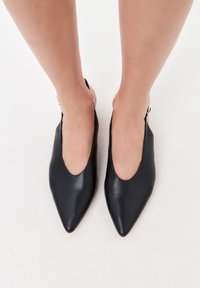Zapatos slingback de cuero negro con punta afilada y lados abiertos. Textura suave y diseño minimalista con un tacón sutil.