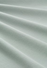 Mint zelena tkanina z teksturirano površino, ki ima mehke gube in gladko, trpežno tkanje. Material se zdi lahek in prožen.