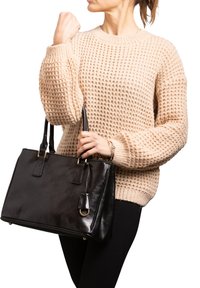 Borsa a mano in pelle nera con hardware dorato, forma rettangolare e manici corti. Maglione beige intrecciato con motivo testurizzato.