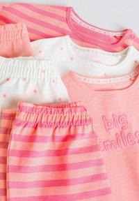 Quatre ensembles de vêtements pour bébé comprenant des hauts roses et blancs assortis à des pantalons à taille élastique, avec des rayures, de petites fleurs et le texte "grands sourires".
