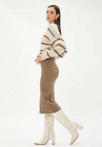 Knit-sweater raido beige ja pruun, millele on kombineeritud sobiv pruun ribatsiooniga seelik ja valged põlvikud. Ühtlane tekstuur läbi kogu komplekti.