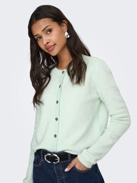 Hellminzgrüner Cardigan aus weichem Stoff, mit Knopfleiste vorne, gerippten Ärmelbündchen und legerem Schnitt. Über dunklem Denim getragen.