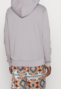 Sudadera con capucha gris de textura suave, combinada con pantalones cortos de colores vibrantes con diseños geométricos en naranja, azul y negro.