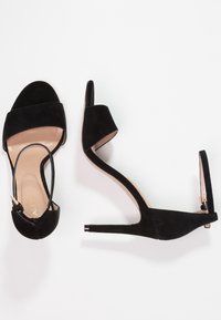 Superbeige korkeahkoluinen sandaalit mustasta nubukista, joissa on leveät hihnat ja säädettävä nilkkahihna. Täysin ohuella stiletto-korkealla ja beigellä sisäpohjalla varustetut.