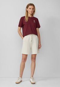 Bordeaux katoenen t-shirt met ronde hals en korte mouwen, gecombineerd met witte, knielange shorts met een elastische tailleband en trekkoord.