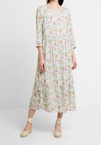 Robe midi fleurie avec des manches trois-quarts, présentant une base blanche ornée de motifs roses, jaunes et verts. Associée à des wedges en espadrille beige.