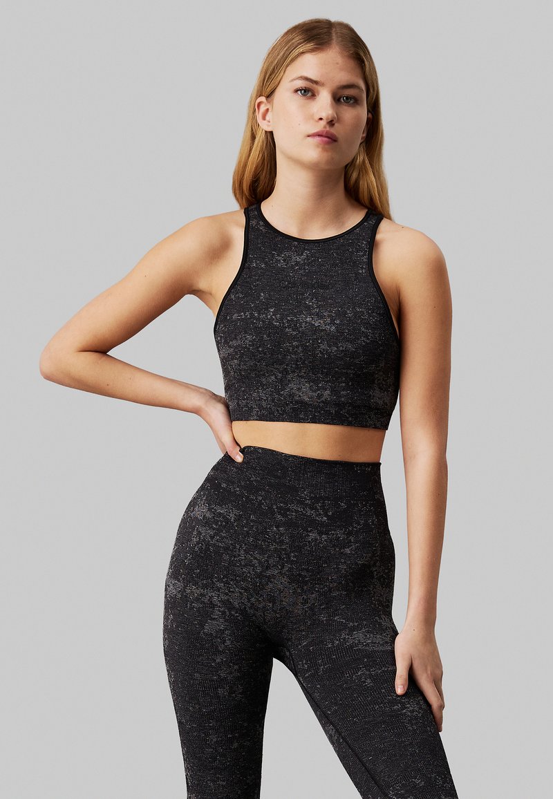 Il crop top sportivo nero e i leggings a vita alta presentano un motivo testurizzato. Il materiale sembra elastico e aderente, adatto per l'abbigliamento attivo.