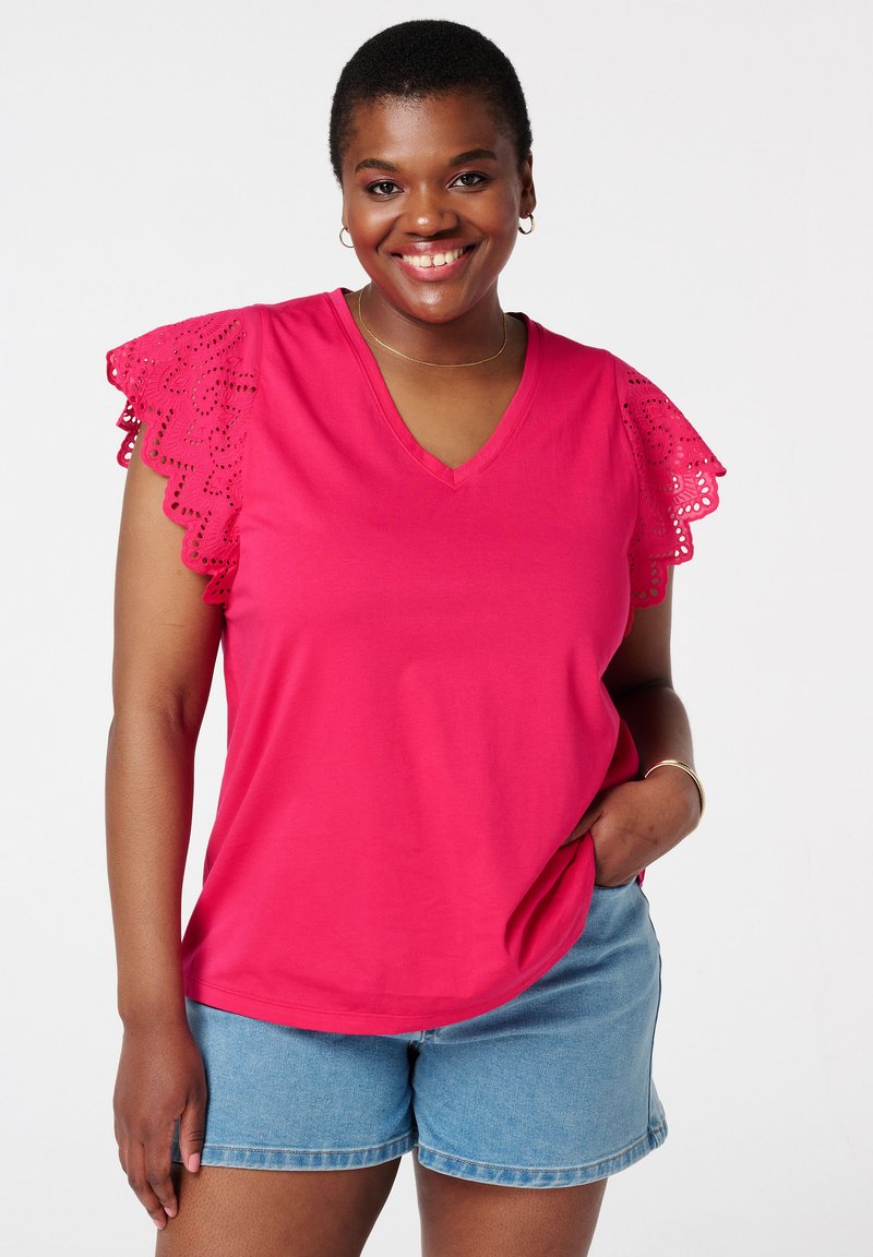 Roze T-shirt met korte mouwen en V-hals, met kanten randjes op de mouwen, gemaakt van zacht materiaal. Gecombineerd met denimbroekjes. Eenvoudig casual design.