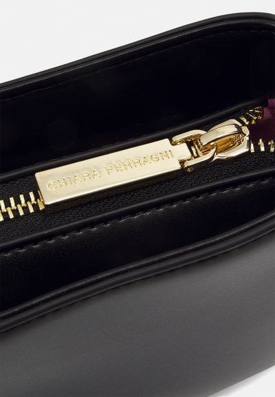 Borsa a mano in pelle nera con zip dorata e linguetta, con il nome del marchio "Chiara Ferragni", caratterizzata da una texture liscia e bordi puliti.