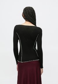 Czarny top z długim rękawem, z białymi przeszyciami i falbaną u dołu. Miękka tkanina przylega do tułowia, z szerokim dekoltem z tyłu.