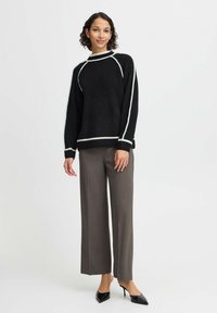 Maglione nero con accenti bianchi, texture morbida, vestibilità ampia; abbinato a pantaloni grigi a gamba larga e tacchi a punta neri.