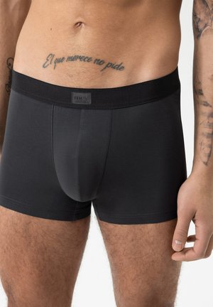 Culottes noires en tissu lisse, avec une large ceinture élastique portant une étiquette de marque. Design ajusté sans motifs.