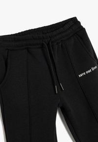 Sorte sweatpants med elastisk talje, snoretræk, sidelommer og trykt tekst "red vores liv" i hvid på venstre lår.