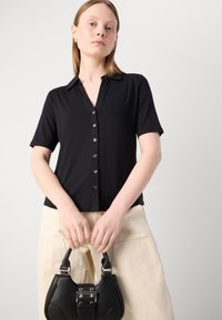 Camicia nera a maniche corte con bottone, realizzata in materiale morbido, con colletto, scollatura a V e cinque bottoni decorativi sul davanti.