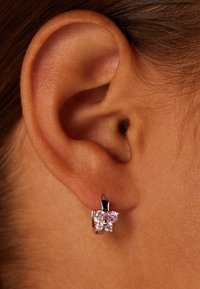 Zilveren ringoorbel met twee decoratieve roze edelstenen in de vorm van een vlinder, naast het oor van een model geplaatst.