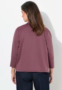 Långärmad topp i mörkrosa med ett svart diamantmönster, slät textur och rund halsringning. Passar bra med mörkblå byxor.