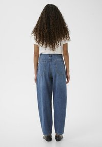 Jeans in denim blu a vita alta con una vestibilità comoda, caratterizzati da due tasche posteriori e un taglio dritto, abbinati a una camicia bianca semplice.