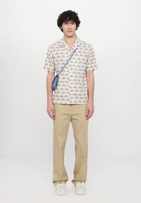Chemise à manches courtes avec un fond clair et un motif de camions colorés. Assortie à un pantalon beige et des baskets. Sac bandoulière inclus.