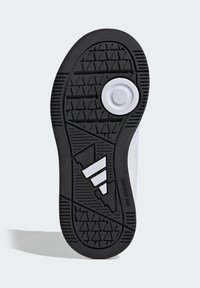 Čierna gumová podrážka topánky s textúrovaným protišmykovým vzorom, s bielymi akcentmi vrátane kruhového emblému a troch diagonálnych pruhov.