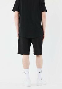 Black cotton t-shirt and black shorts; white sneakers and socks with black accents; minimalistic design; smooth fabric texture.