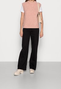 Jasnoróżowy dzianinowy top bez rękawów na białej koszulce, w połączeniu z czarnymi spodniami o szerokich nogawkach i beżowymi butami na masywnej podeszwie; subtelna faktura.