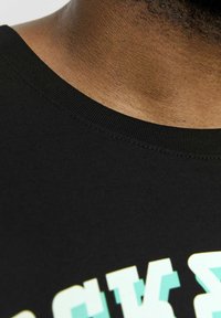 Schwarzes Baumwoll-T-Shirt mit rundem Halsausschnitt, mit auffälligem aqua und weißem Text am unteren Rand. Nahaufnahme der Stoffstruktur und Nähte.