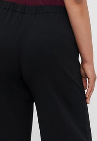 Pantalones con cintura elástica negra y textura suave, que presentan un corte relajado. El material parece suave y cómodo, adecuado para el uso casual.