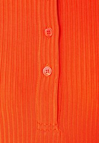 Helle orange gestreifte Stoff mit zwei rosafarbenen Knöpfen entlang der Knopfleiste. Glatte Textur mit sichtbaren Nähten und einem nahtlosen Finish.
