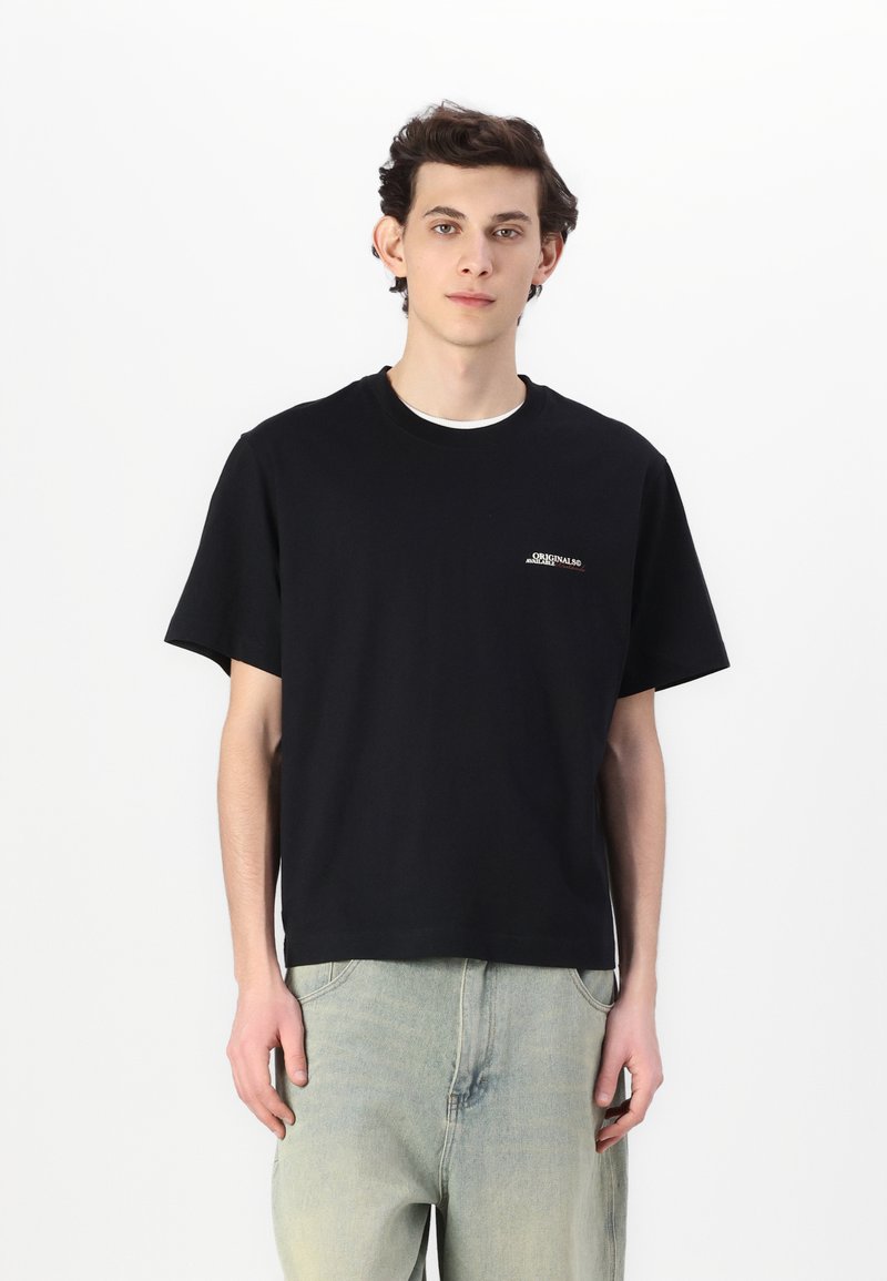 Schwarzes Baumwoll-T-Shirt mit kurzen Ärmeln und Rundhalsausschnitt, mit weißen Logo-Details auf der Brust, kombiniert mit hellblauen Jeans.