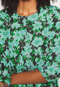 Vestido floral con grandes flores azul claro y hojas verdes sobre un fondo negro texturizado. Las mangas están fruncidas en los puños.