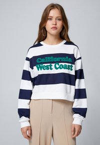 Sudadera a rayas en azul marino y blanco con texto bordado en verde "California West Coast". Diseño cropped, puños acanalados y cuello redondo.