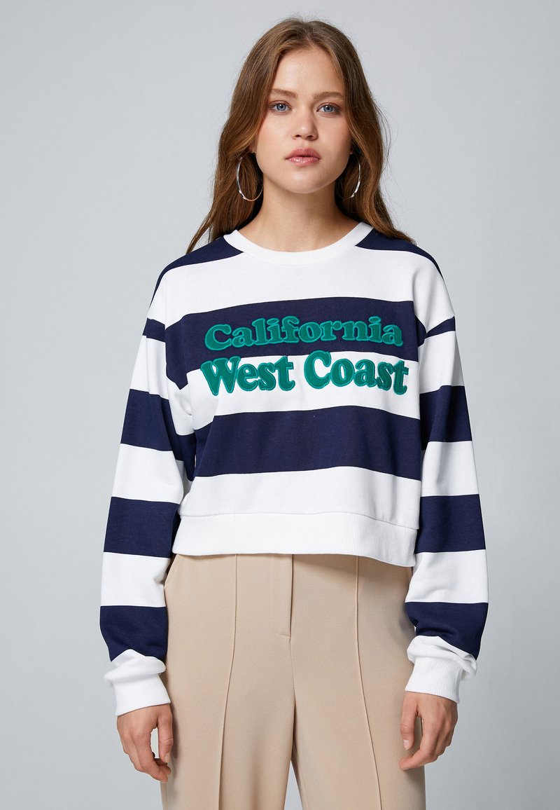 Sudadera a rayas en azul marino y blanco con texto bordado en verde "California West Coast". Diseño cropped, puños acanalados y cuello redondo.