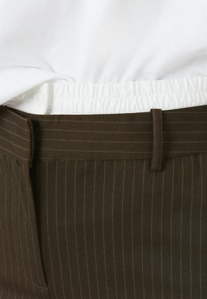 Pantalons marron à rayures fines avec une taille plate, une ceinture élastique et un tissu intérieur blanc contrastant qui ressort en haut.