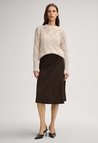 Lichtbeige gebreide trui met open steekpatroon, gecombineerd met een donkerbruine suède midi rok en zwarte slingback hakken.