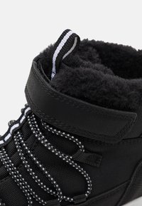 Schwarzer High-Top-Schuh mit strukturierter Oberfläche, gefüttert mit einem weichen Innenfutter, kontrastierenden weißen Akzenten und elastischen Schnürsenkeln mit einer Zuglasche.