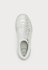 Zapatilla deportiva blanca con un exterior de cuero brillante, cierre con cordones, cuello acolchado y laterales texturizados que presentan un logotipo y patrones bordados.