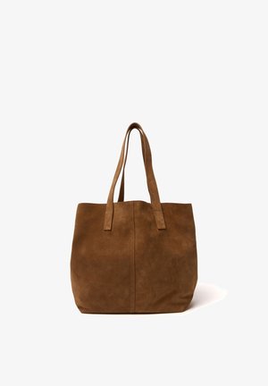 Bolso tote de ante marrón con dos asas largas, textura suave y diseño sencillo, de pie sobre un fondo blanco.