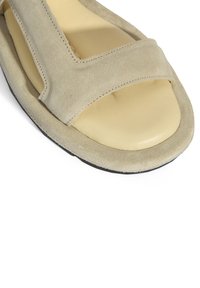 Suède slipper sandaal in lichtbeige met een brede V-vormige band en een comfortabele beige binnenzool, met een zwarte rubberen buitenzool.