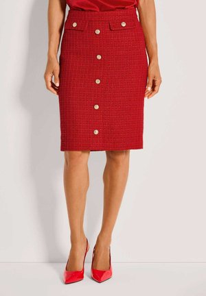 Roter knielanger Rock mit strukturierter Oberfläche und goldfarbenen Knöpfen vorne, zwei Klappentaschen, kombiniert mit passendem rotem Oberteil und roten spitzen High Heels.