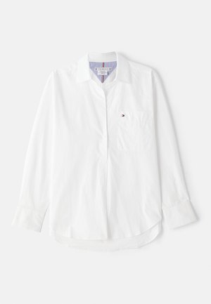 Valge pika varrukaga särk, mis on valmistatud puuvillast, nööbiga krae, rinnatasku ja peened triibud krae sees.