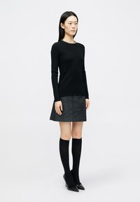 Μαύρο πουλόβερ με μακριά μανίκια και ριμπ ύφανση, συνδυασμένο με σκουρόχρωμη τζιν φούστα. Το μοντέλο φοράει μαύρες κάλτσες μέχρι το γόνατο και μυτερές γόβες.