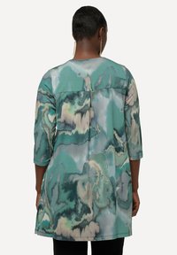 Lange tuniek met een vloeiend, abstract patroon in tinten groen en crème, met driekwartmouwen en een effen achterpaneel.