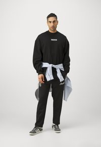 Sudadera negra con el texto "JUVENTUS", pantalones joggers negros con logo, camisa a rayas azul clara atada a la cintura y zapatillas a rayas grises.
