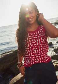 Gehaakt tanktop met rood-witte vierkantpatronen, voorzien van een ronde halslijn en verfijnde details. Gecombineerd met donkerblauwe korte broek.