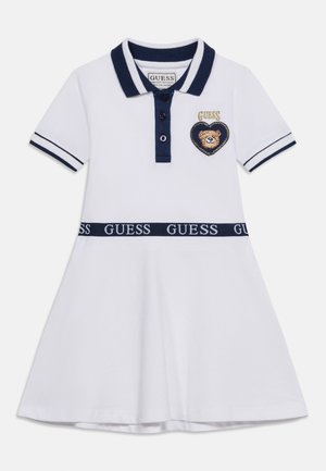 Bela polo obleka s kratkimi rokavi, mornarsko modrim ovratnikom, gumbi na prednjem delu, pasom z napisom "GUESS" in srčnim motivom z obrazom medvedka na prsih.