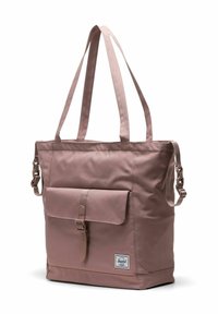 Sac fourre-tout rectangulaire rose poussiéreux avec poche avant à boucle, deux longues bandoulières et petite étiquette de marque près de la base.