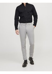 Czarna koszula zapinana na guziki z długimi rękawami, w połączeniu z jasnoszarymi spodniami slim-fit. Spodnie maj�ą kieszenie i zapinane są na guzik z przodu. Czarne buty.