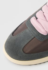 Hallid hall suède ja kangast sneaker roosa paelaga, ümar varvas ja kontrastne kummitald. Nähtavad silmapaistvad õmblused ja võrkkangast elemendid.